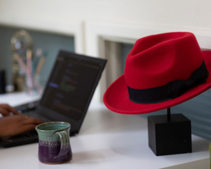 A red hat on a stand next to a laptop as someone types