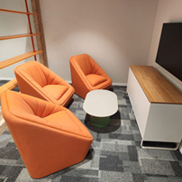Small discussion space with orange chairs and a screen.