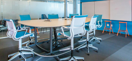Bright makerspace or collaboration area with a large light-colored oval table, blue and white chairs