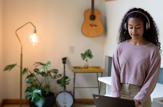 A woman uses a laptop with various musical instruments in the background