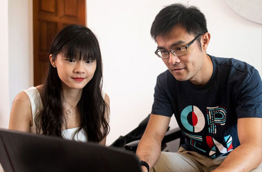 Two people look at a laptop screen with a brown door behind them