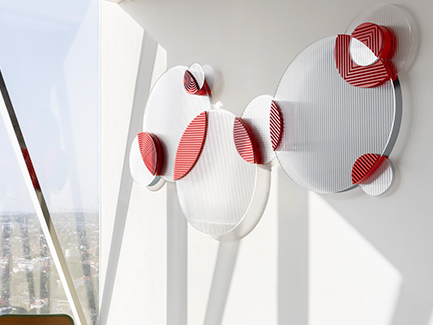 Transparent circular wall art with red accents on a white wall in bright natural light