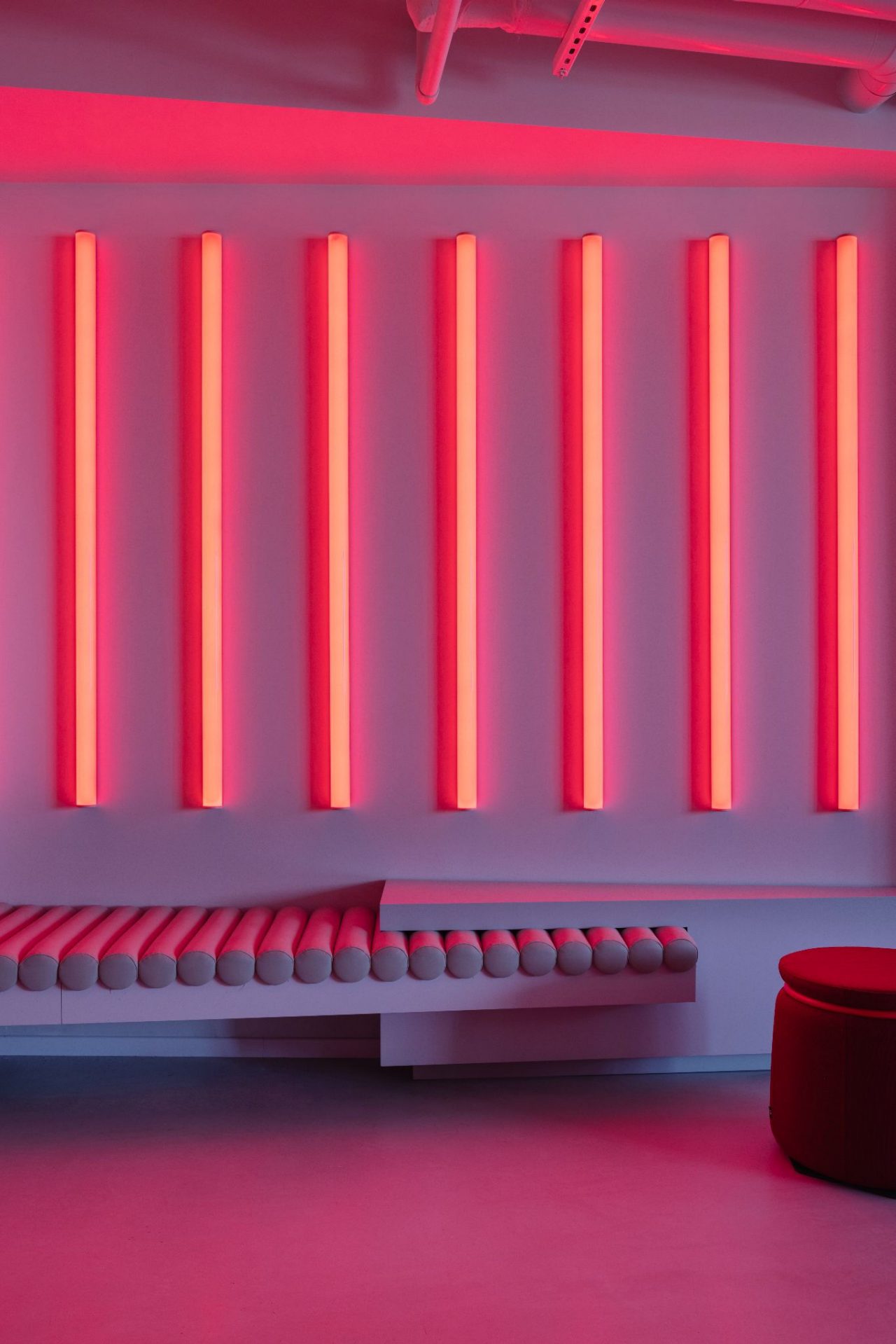 a series of glowing red neon vertical neon lights side by side on a white wall