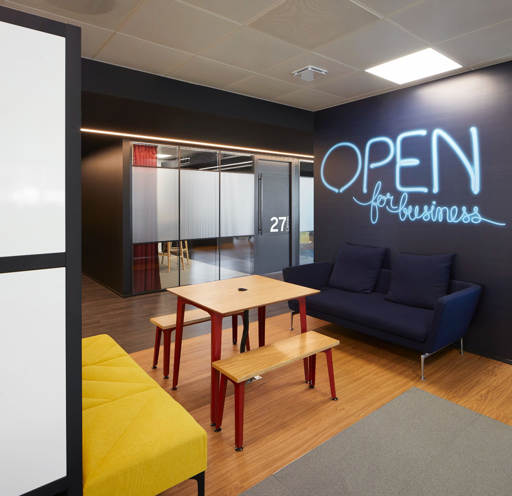 a common area featuring a dark blue wall with large light blue neon signage reading Open for business