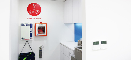 A compact office corner designated as a "Safety Spot" with a first aid kit, fire extinguisher, and AED next to a printer and counter.