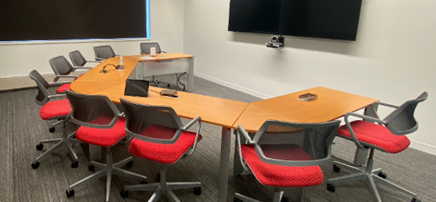 ference room with a long wooden table, red and grey chairs, a large wall-mounted screen, and whiteboards