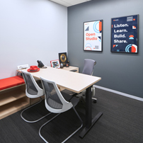 Modern meeting room with a rectangular table, three chairs, bench seating, and inspirational posters on the wall
