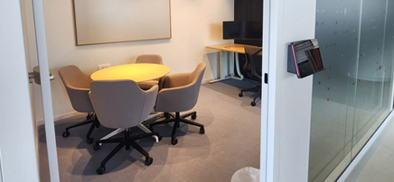 Small meeting room with a round table, four chairs, a whiteboard, and glass walls