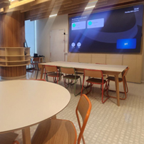 Office pantry space with round light wood tables, matching chairs, and large windows