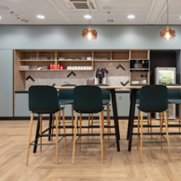 Office breakroom with a long high-top table, black stools, and a large presentation screen on the wall