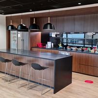 Modern office kitchen area with light wood cabinetry, a long white counter, and integrated appliances