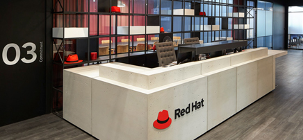 Angled view of a white and wood-tone reception desk with a 'Red Hat' logo