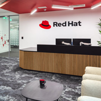Dark, ribbed reception desk with a 'Red Hat' logo on a white wall, in front of a patterned carpet