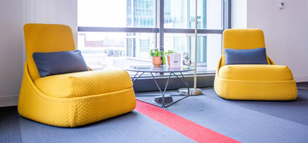 Two bright yellow modern lounge chairs in a well-lit office space with large windows