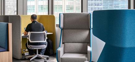 Individual privacy pods or high-back chairs in an office setting near a window
