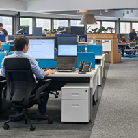 Open-plan office with rows of desks and a glass partition